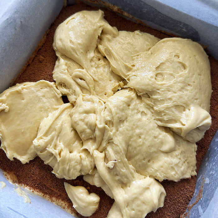 Unbaked sourdough coffee cake batter dolloped onto walnut-cinnamon crumble in a parchment-lined square pan