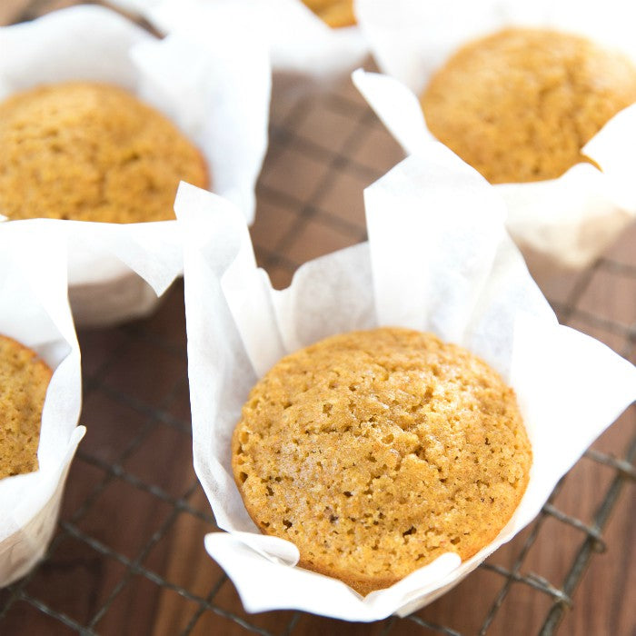 Overhead close-up of an Einkorn corn muffin in a parchment liner showing a golden domed top and tender crumb on a wire cooling rack