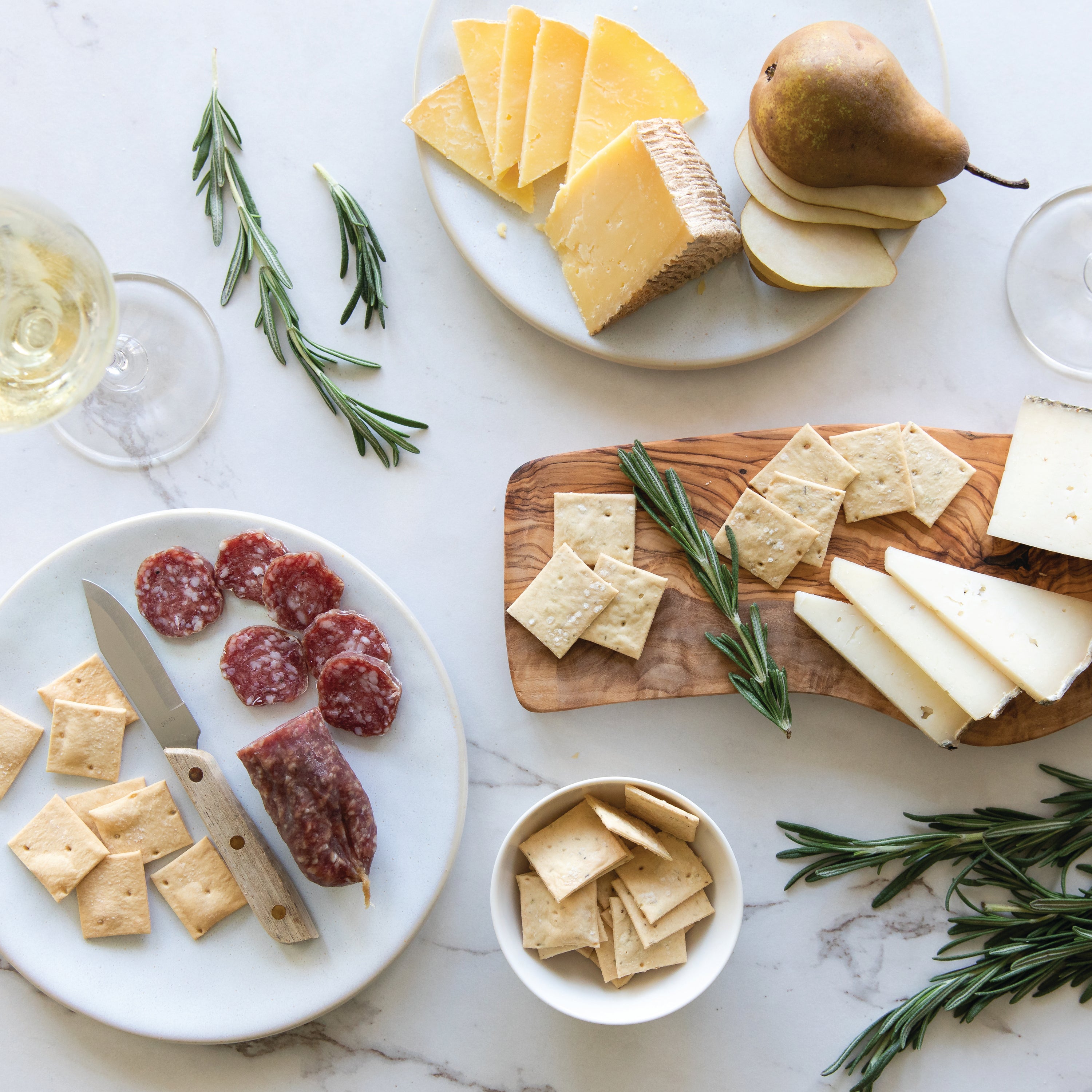 Charcuterie spread with Organic Einkorn rosemary sourdough crackers, sliced cheeses, salami, pear, and rosemary sprigs on a marble surface