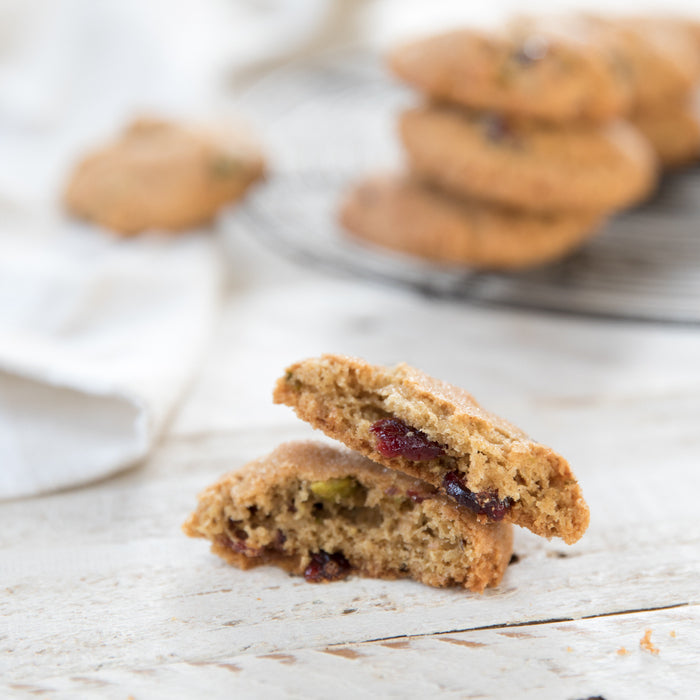 Close up of einkorn cranberry pistachio cookie split to show chewy interior with cranberries and pistachios on white wood
