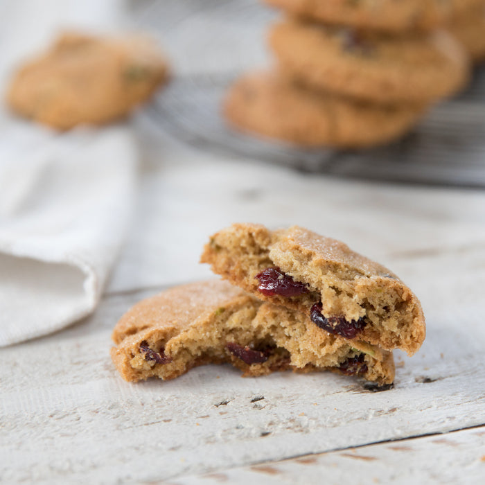 Close-up of a broken Einkorn cranberry-pistachio cookie showing dried cranberries and pistachio pieces on a white wooden surface