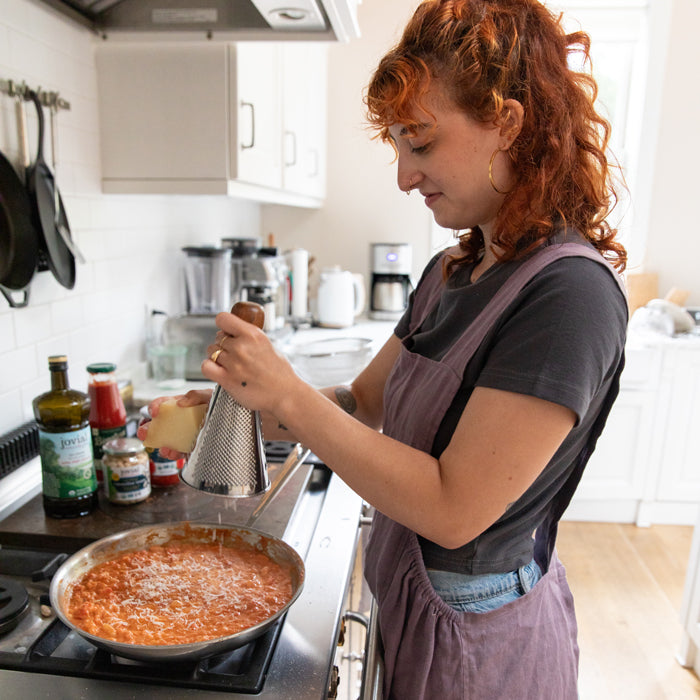 Woman grating cheese over a skillet of creamy cannellini beans and tomato sauce in a bright home kitchen