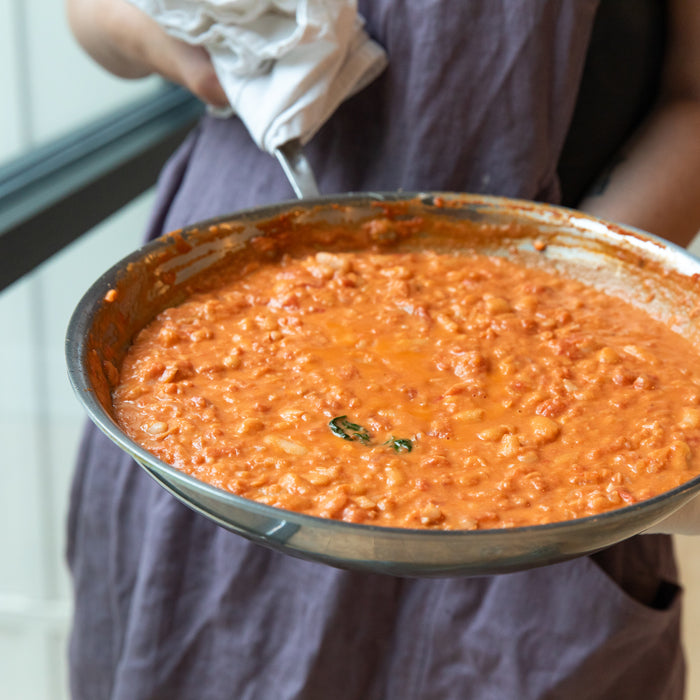 Person holding skillet of creamy white bean and tomato stew near a sunlit window