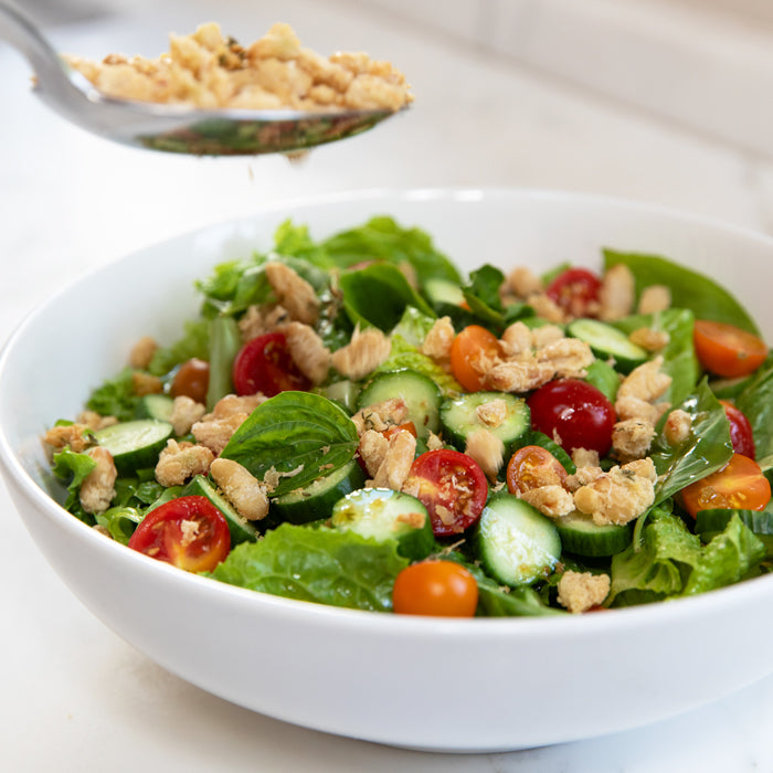 Salad topped with crispy organic cannellini beans, cherry tomatoes, cucumber slices, and mixed greens in a white bowl