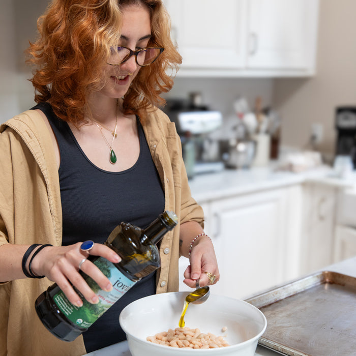 Person pouring extra virgin olive oil over cannellini beans in a white bowl on a home kitchen counter