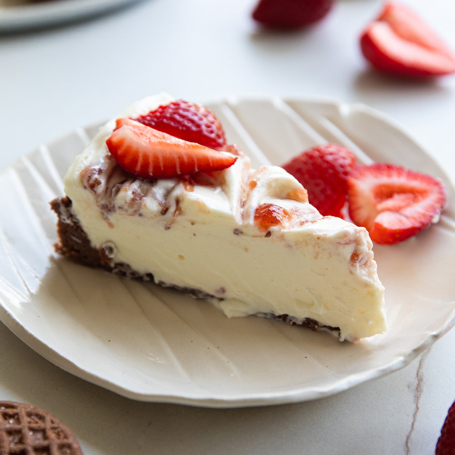 Side view of a slice of Crispy Cocoa No-Bake Cheesecake showcasing creamy filling, Einkorn crispy cocoa cookie crust, and sliced strawberries on a white plate