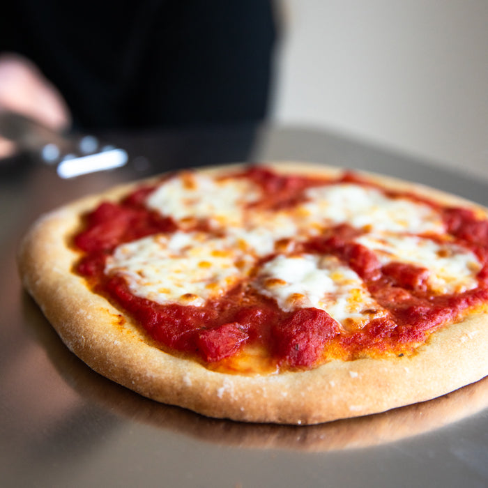 Close up of pizza on a metal peel showing einkorn crust topped with organic crushed tomato sauce and melted mozzarella