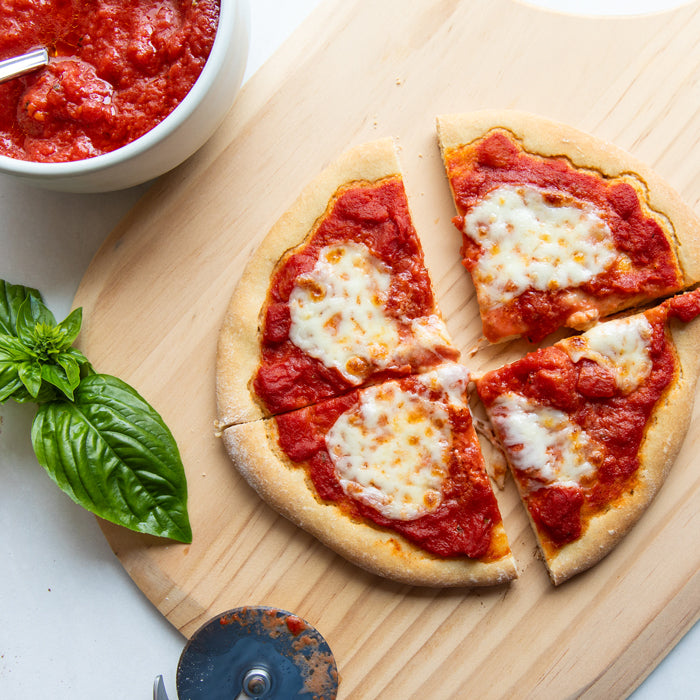 Overhead view of a four-slice pizza with crushed tomato sauce and mozzarella on einkorn crust, bowl of sauce and basil