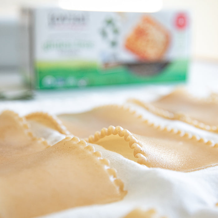 Close-up of uncooked gluten-free lasagna sheets showing ruffled edges and smooth surface with a blurred Jovial box in the background