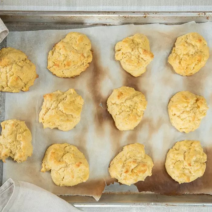 Overhead view of twelve Einkorn butter drop biscuits with golden cracked tops on a parchment-lined baking sheet