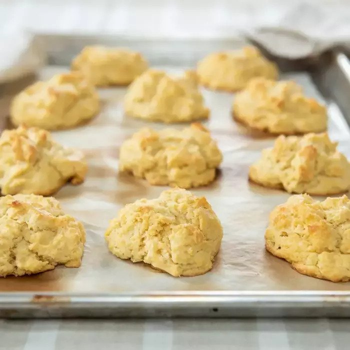 Angled view of baked Einkorn butter drop biscuits with golden rustic tops on a parchment lined rimmed baking sheet