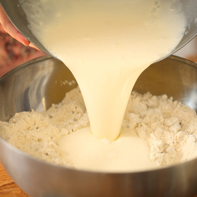 Buttermilk being poured into a bowl of einkorn flour to make Irish soda bread