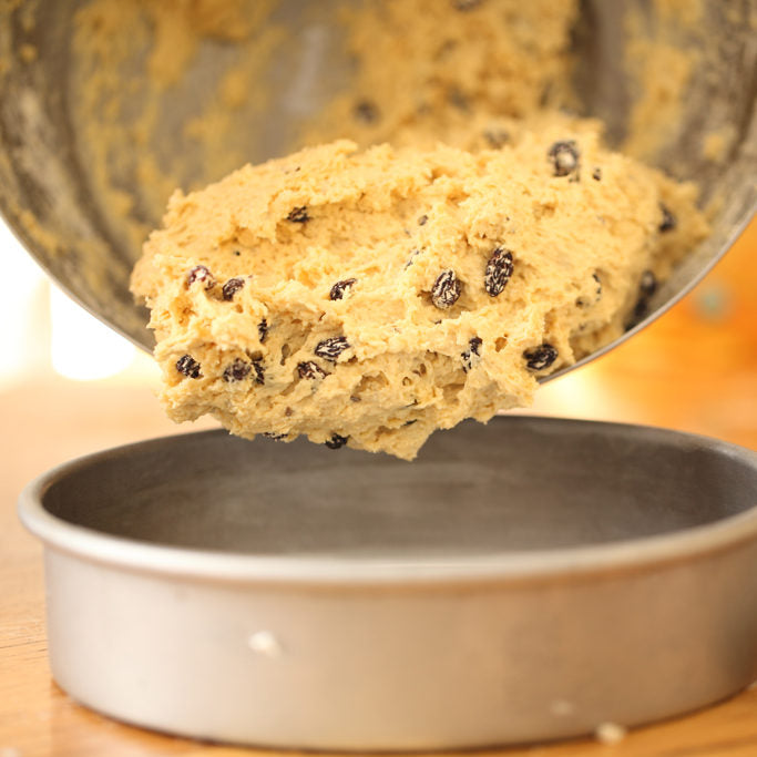 Einkorn Irish soda bread dough with raisins being scraped from a mixing bowl into a round baking pan