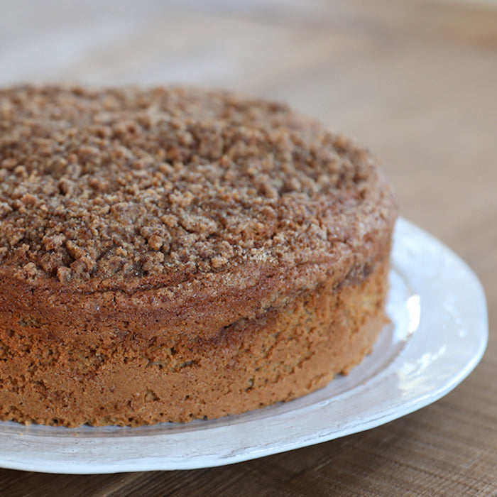 Close-up three-quarter view of Einkorn sour cream coffee cake with cinnamon streusel on a white plate over a wooden table