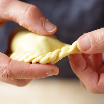 Close-up of hands crimping an empanada made with einkorn dough in a home kitchen