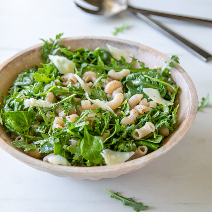 Bowl of organic gluten-free brown rice pasta tossed with arugula and shaved Parmesan on a light marble surface
