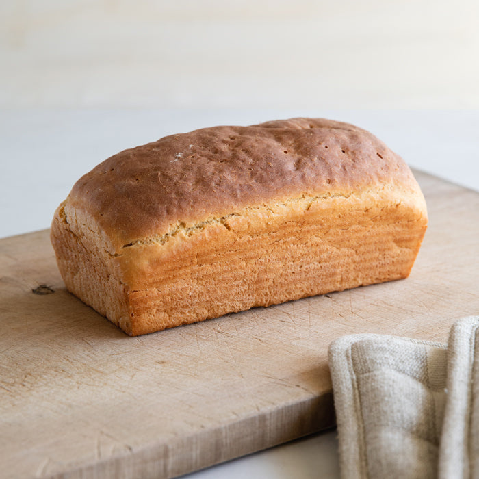 Three-quarter view of organic Einkorn sandwich loaf showing golden crust and soft crumb on a wooden cutting board with a linen cloth