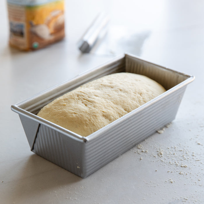Angled view of unbaked Einkorn sandwich loaf dough rising in a metal loaf pan on a floured countertop