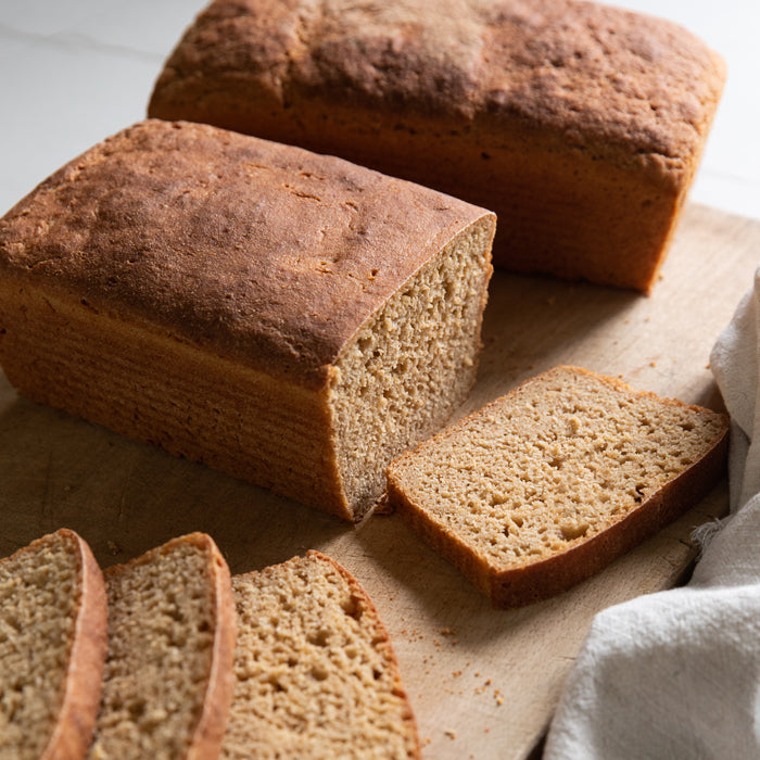 Three-quarter view of whole-grain einkorn loaf showcasing sliced dense crumb on a wooden board with a linen cloth