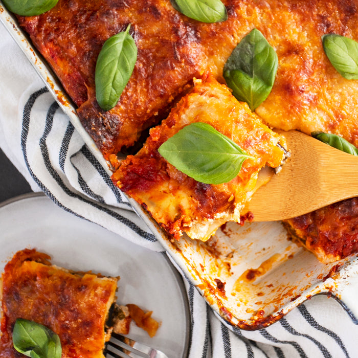 Baked eggplant lasagna being served from a ceramic baking dish onto a plate, topped with fresh basil