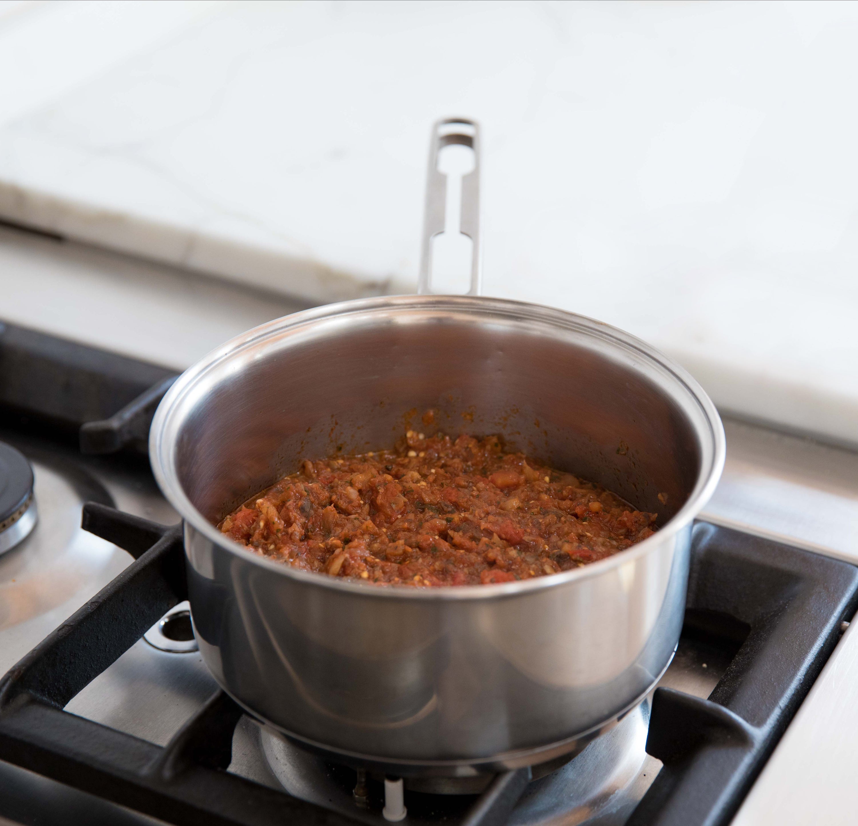 Chopped eggplant and mushroom tomato sauce simmering in a stainless saucepan on a gas stove