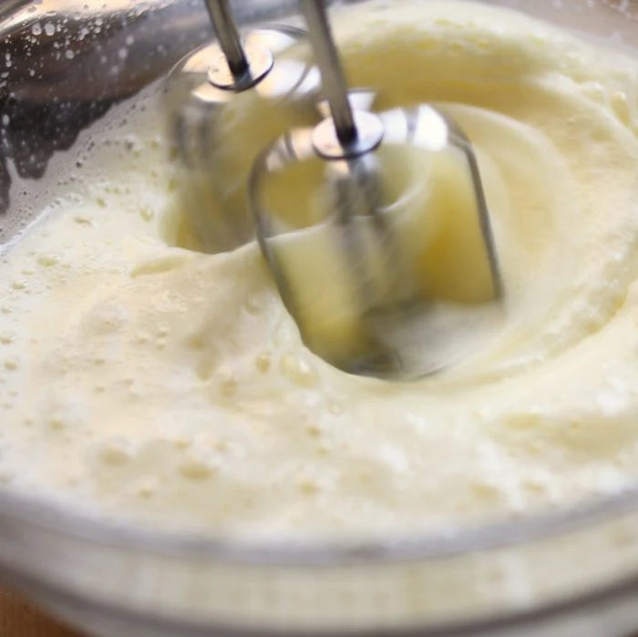 Hand mixer whipping eggs and sugar into a light, fluffy batter for olive oil cake in a glass bowl