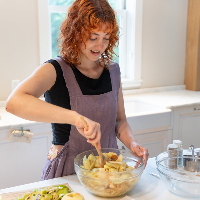 Home cook mixing sliced apples in a glass bowl to make a crunchy Einkorn apple crumble in a bright kitchen