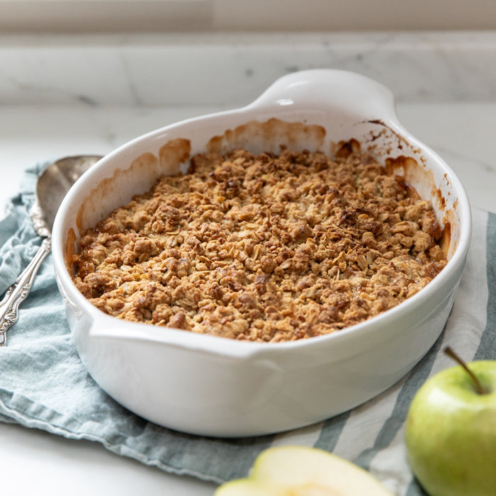 Top-down view of Einkorn apple crumble in a white baking dish with golden crunchy topping and green apples