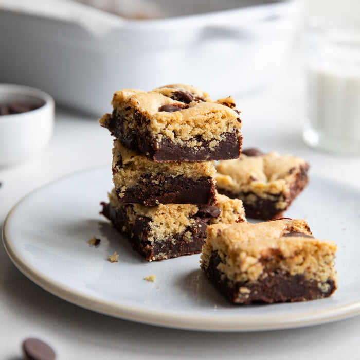 Stacked Einkorn brookies with fudgy chocolate brownie layer and golden cookie top on a plate, baking dish blurred behind