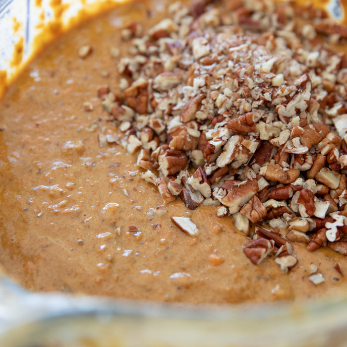 Close-up of einkorn carrot cupcake batter in a glass bowl with chopped pecans on top