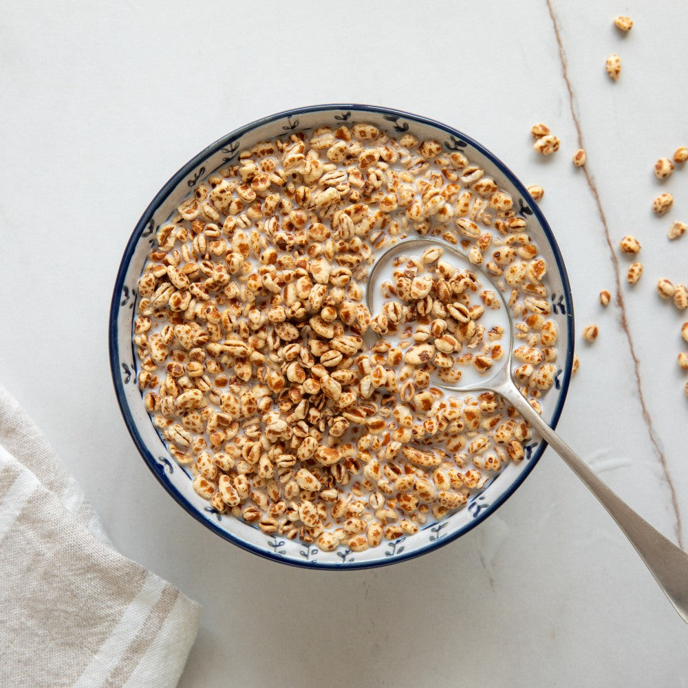 Overhead view of two bowls of organic Einkorn cereal puffs with spoons on a light countertop, simple breakfast setting