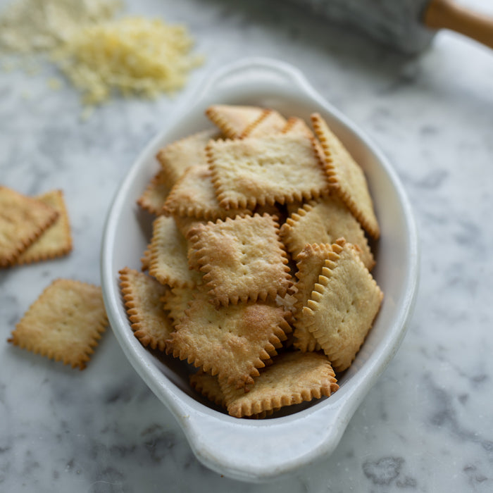 Overhead view of Cheddar Einkorn crackers in a white dish showcasing golden brown edges and crimped squares on marble counter