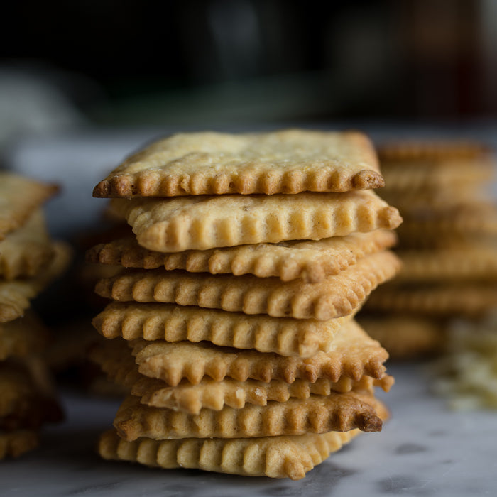 Close-up view of a stack of Cheddar Einkorn crackers showing golden scalloped edges and flaky texture on a marble surface
