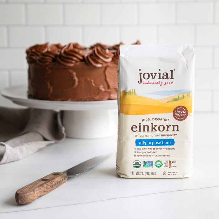 Front view of Jovial Einkorn all-purpose flour bag showing 100% organic label with chocolate cake on a white stand in background