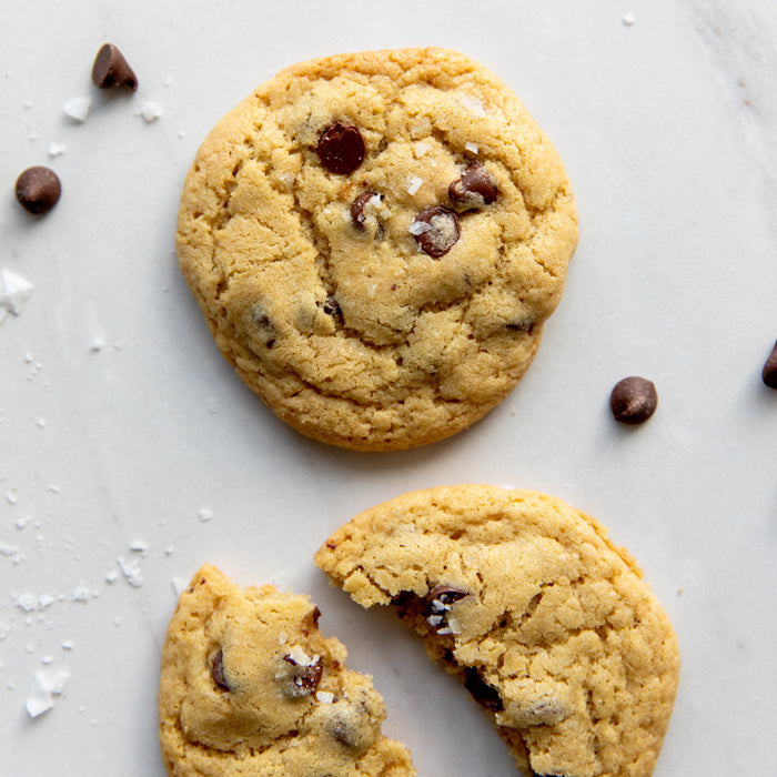 Top-down view of Einkorn chocolate chip cookies, one broken to show soft interior and chocolate chips, with flaky sea salt