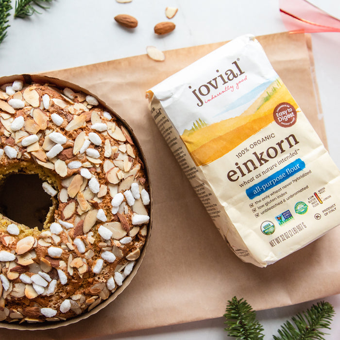 Top-down view of bag of Jovial Einkorn flour beside Italian Christmas cake topped with sliced almonds and pearl sugar