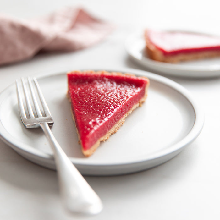 Close-up of a slice of Einkorn cranberry tart showcasing glossy deep-red filling and golden einkorn crust on a white plate