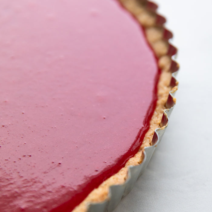 Close-up of an Einkorn cranberry tart in a fluted pan with glossy red cranberry filling and a golden einkorn crust