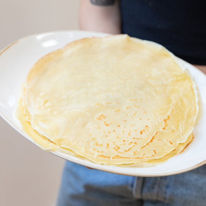 Stack of golden einkorn crêpes on a white plate held by a person against a neutral background