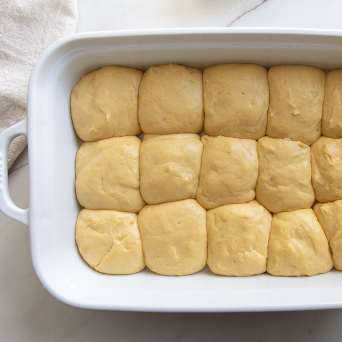 Raw einkorn roll dough balls arranged in a white rectangular baking dish ready for baking