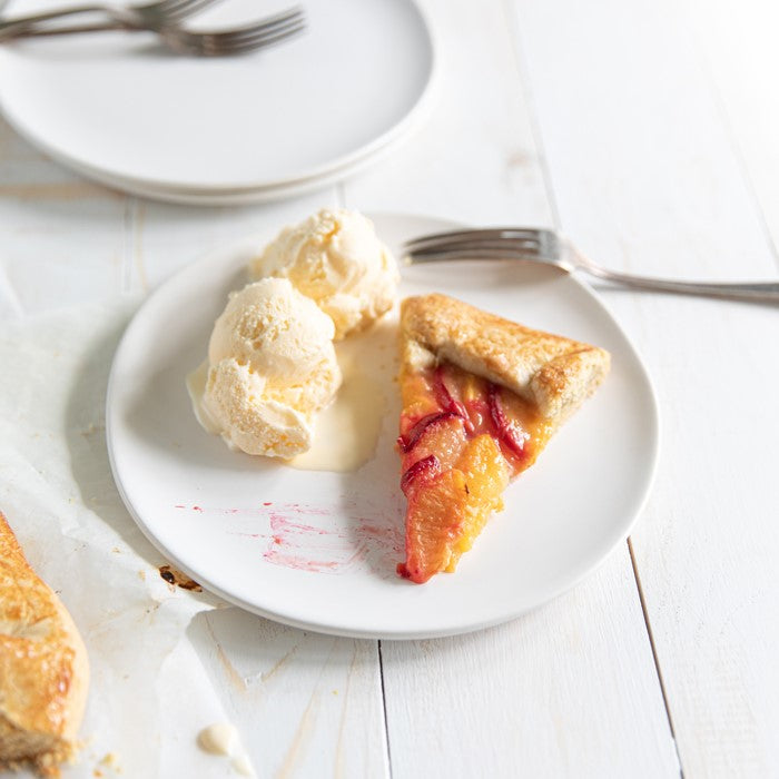Overhead view of Einkorn fruit galette slice showcasing peach and plum filling with vanilla ice cream on a white plate