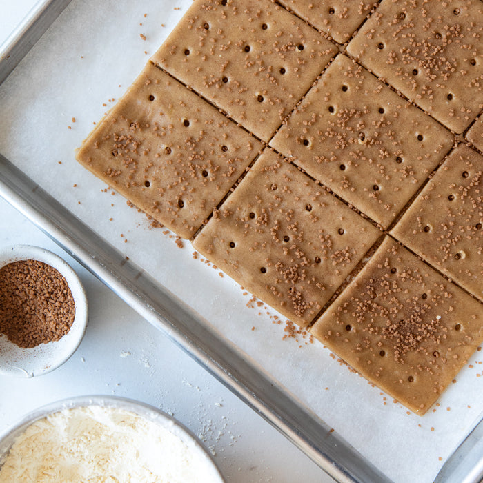 Overhead view of unbaked Einkorn graham crackers scored into squares with coarse brown sugar on a parchment lined baking sheet