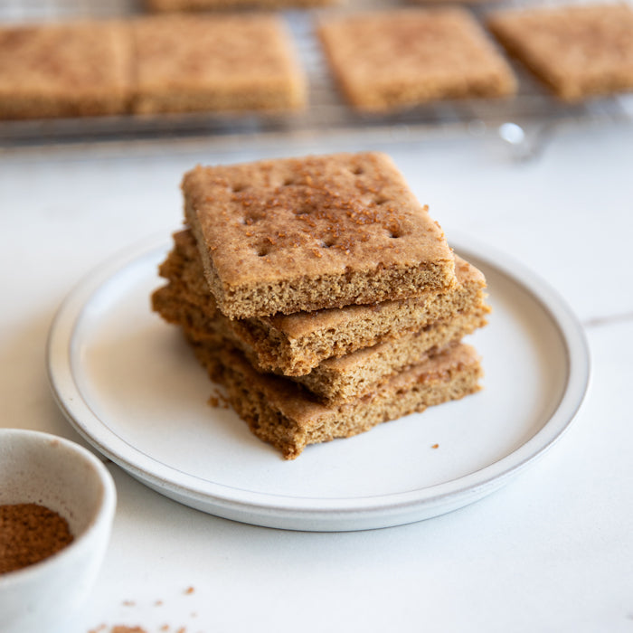 Close-up of stacked Einkorn graham crackers showing crumbly texture and cinnamon sugar on a white plate and cooling rack