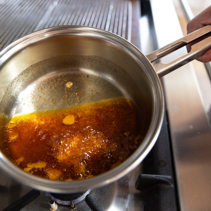 Butter and chili oil simmering in a stainless steel saucepan on a gas stove for lobster roll filling