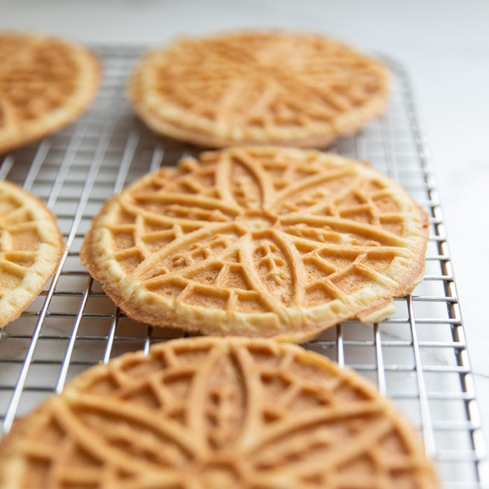 Close-up of einkorn pizzelle on a cooling rack showcasing decorative star pattern and golden edges with gray background