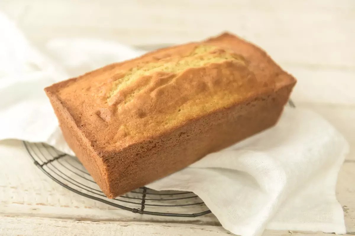Three-quarter view of an Einkorn pound cake showing a golden crust and top crack on a wire cooling rack with white linen