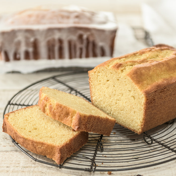 Sliced Einkorn pound cake showing moist crumb and golden crust on a wire cooling rack with a glazed loaf in background