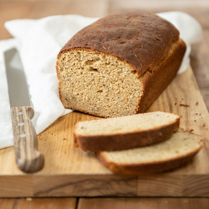 Three-quarter view of an Einkorn rye loaf with dense crumb and golden-brown crust on a wooden board, two slices and a knife