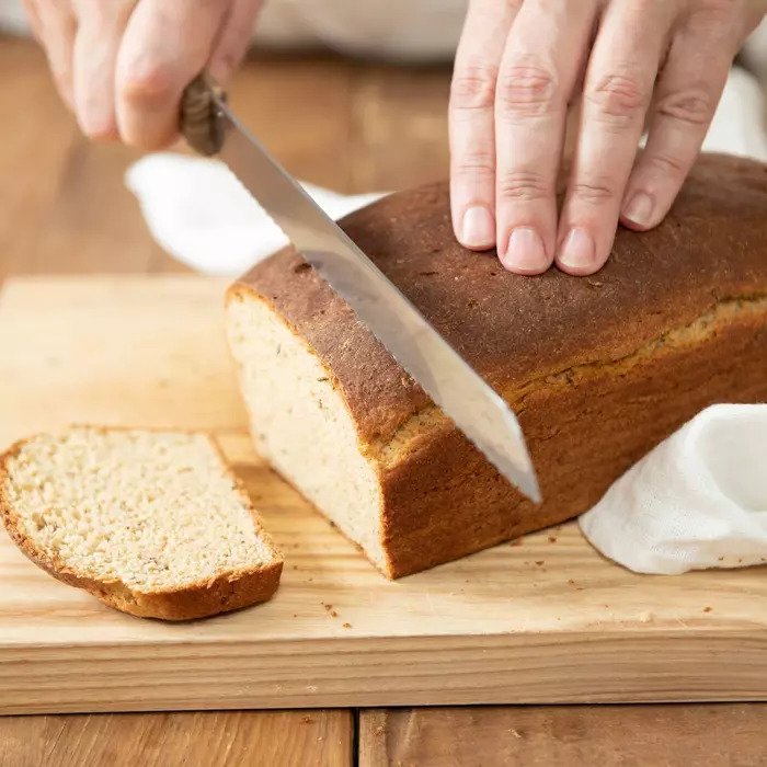 Angled close-up of a sliced loaf of Einkorn rye bread showcasing dense crumb and golden crust on a wooden cutting board