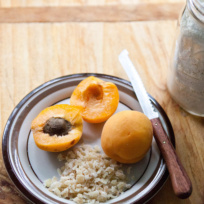 Apricot halves and chopped crystallized ginger on a plate with knife and jar of flour, ingredients for Einkorn scones